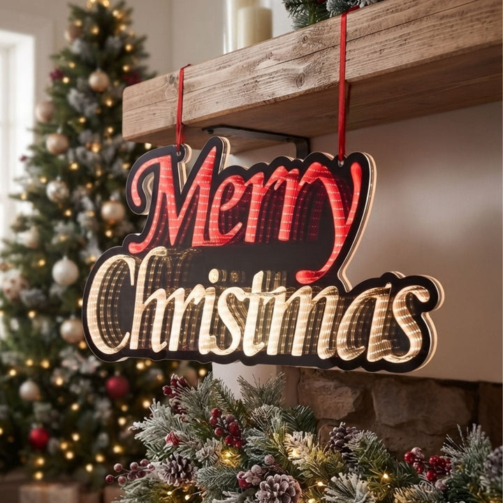 A decorative hanging Christmas sign with red and cream lettering that reads “Merry Christmas,” suspended by red ribbons in front of a fireplace with a decorated tree in the background.