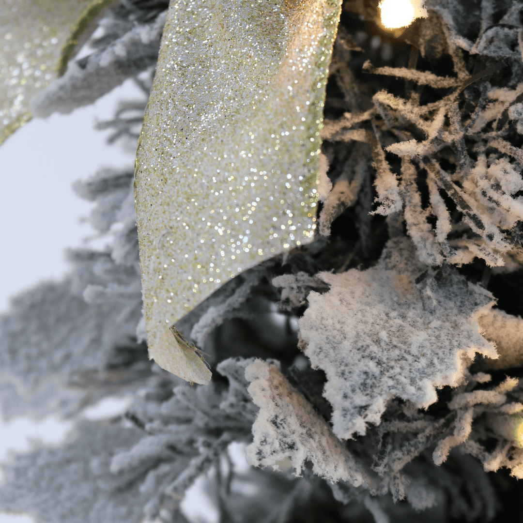 detail shot of holly shaped branches covered in snow on christmas tree