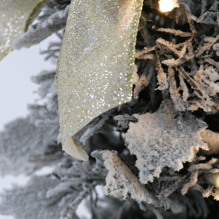 detail shot of holly shaped branches covered in snow on christmas tree