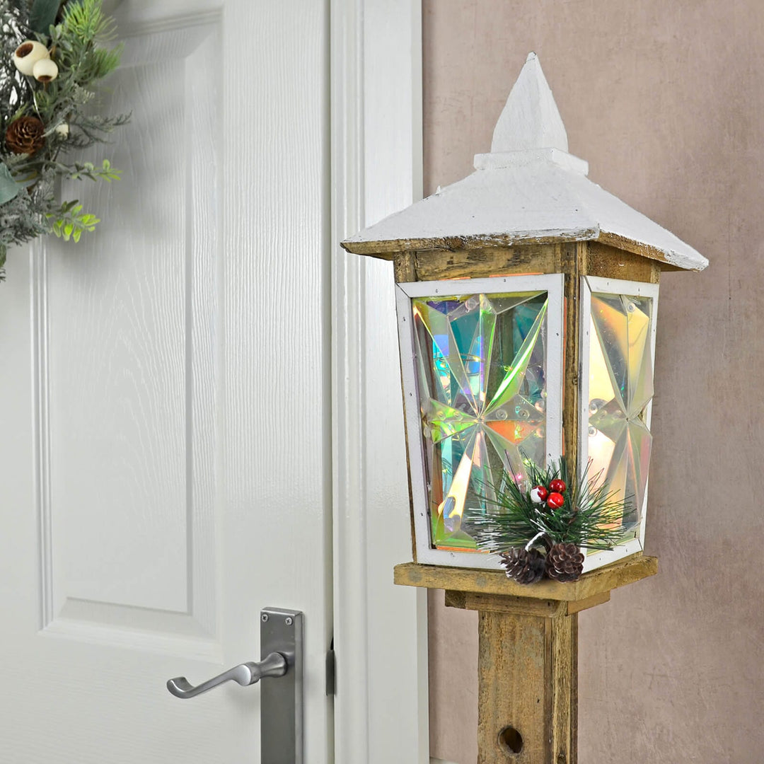 Close up of light up lantern with wooden post pine cones berries and door with Christmas wreath