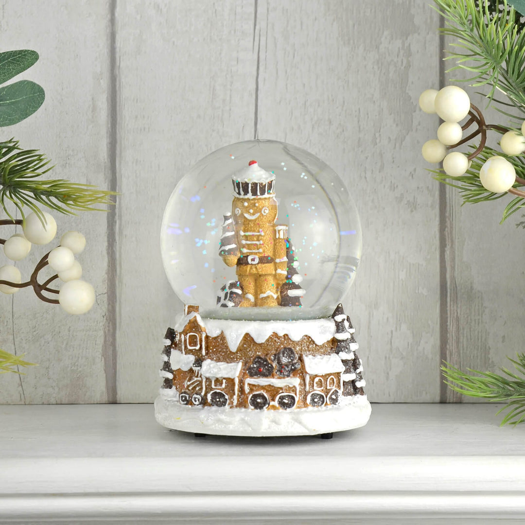 Gingerbread man nutcracker snow globe with train on a wooden surface with Christmas foliage.