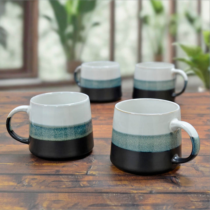 Four large porcelain mugs with white blue and black on a wooden table with plants.