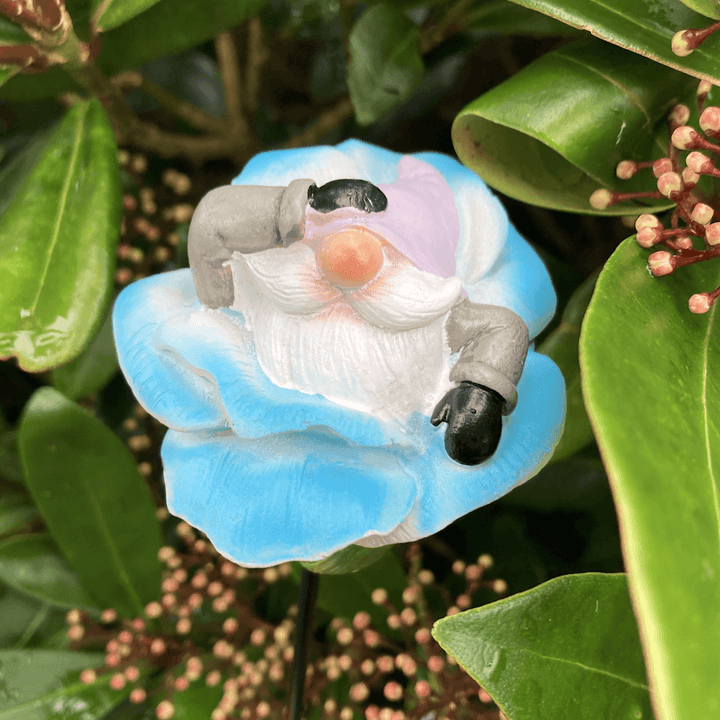 gnome stake with blue flower and lilac hat in outdoor foliage