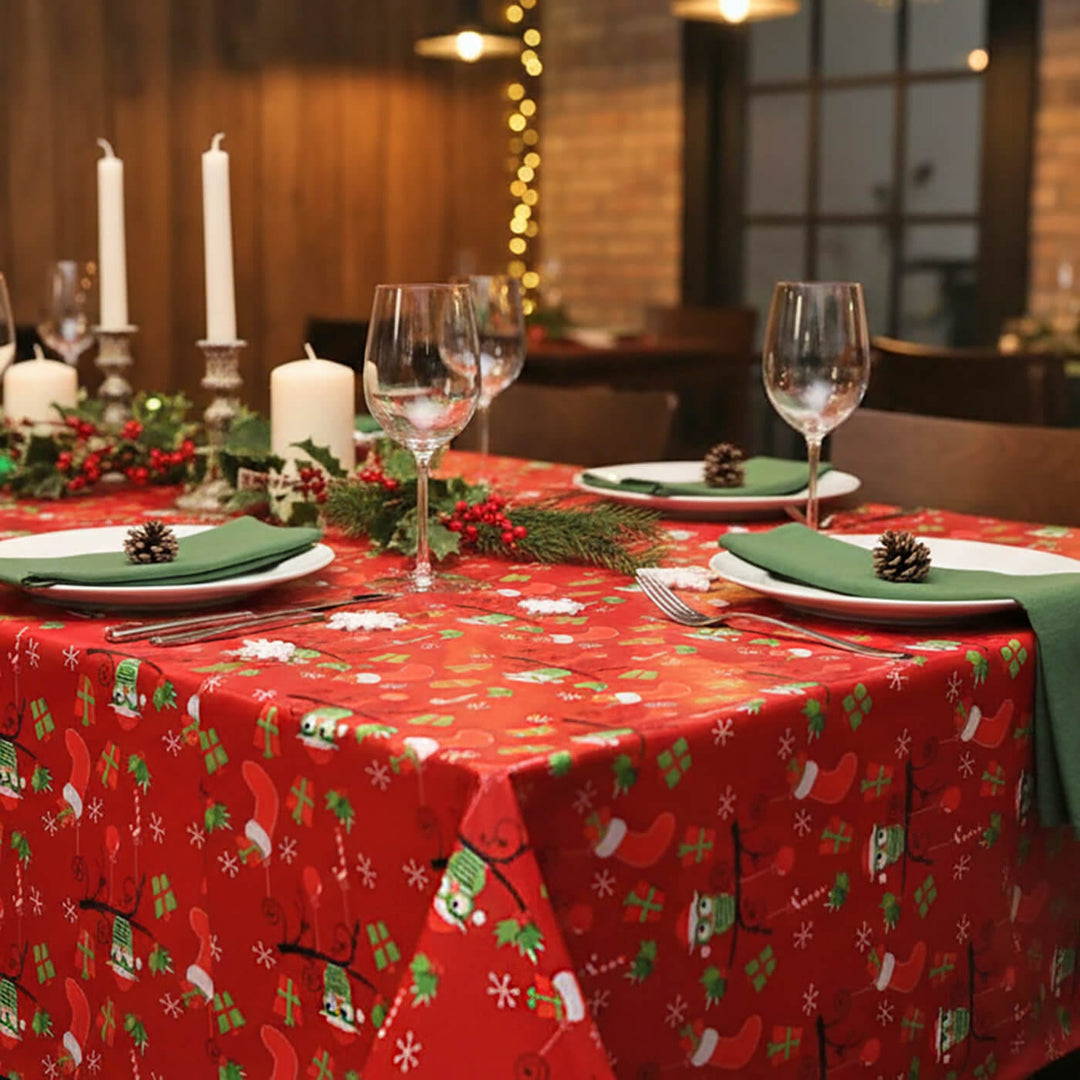 Dining table set for Christmas with a red patterned tablecloth, white candles, and glassware.