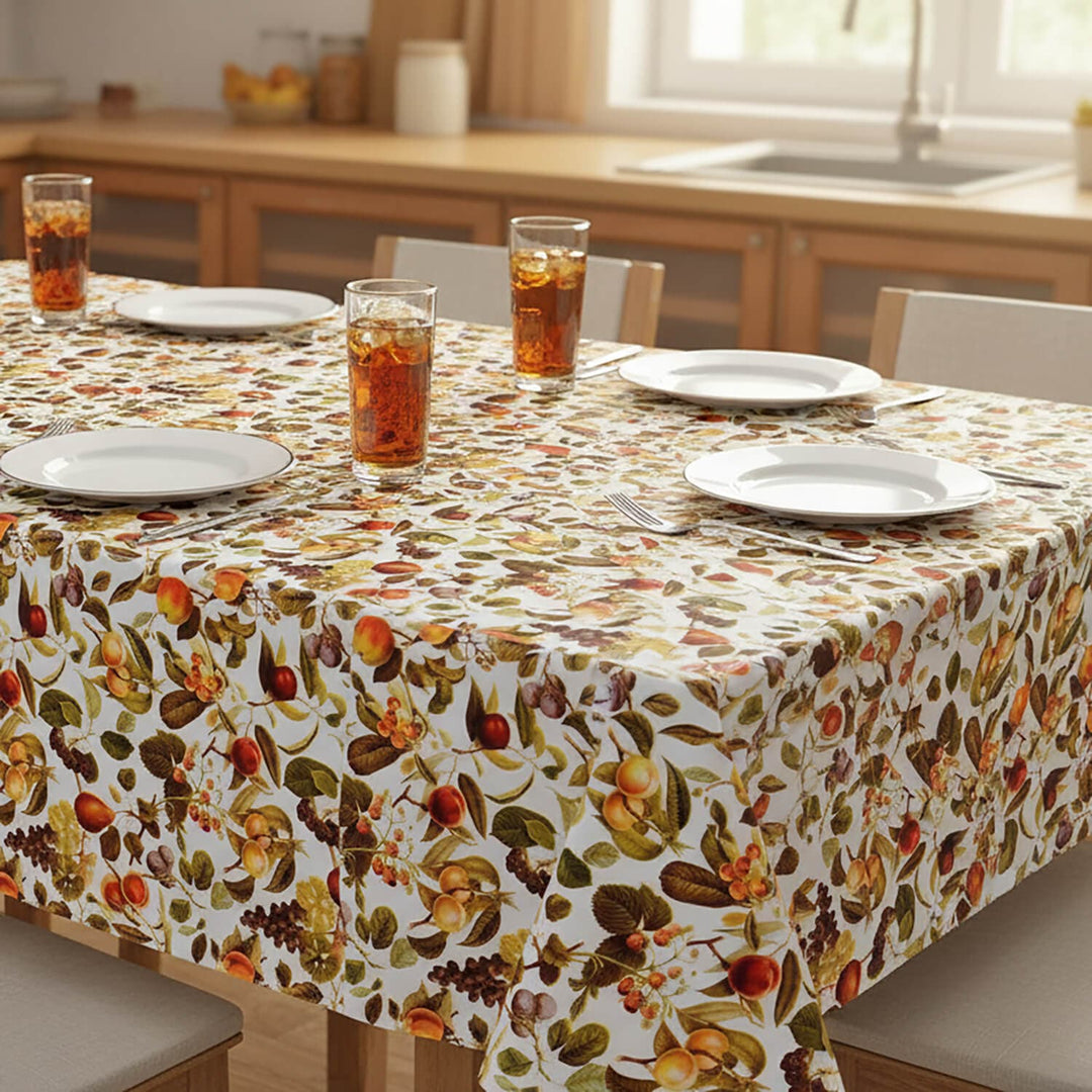 Dining table set with a fruit pattern tablecloth, plates, and glasses in a kitchen.